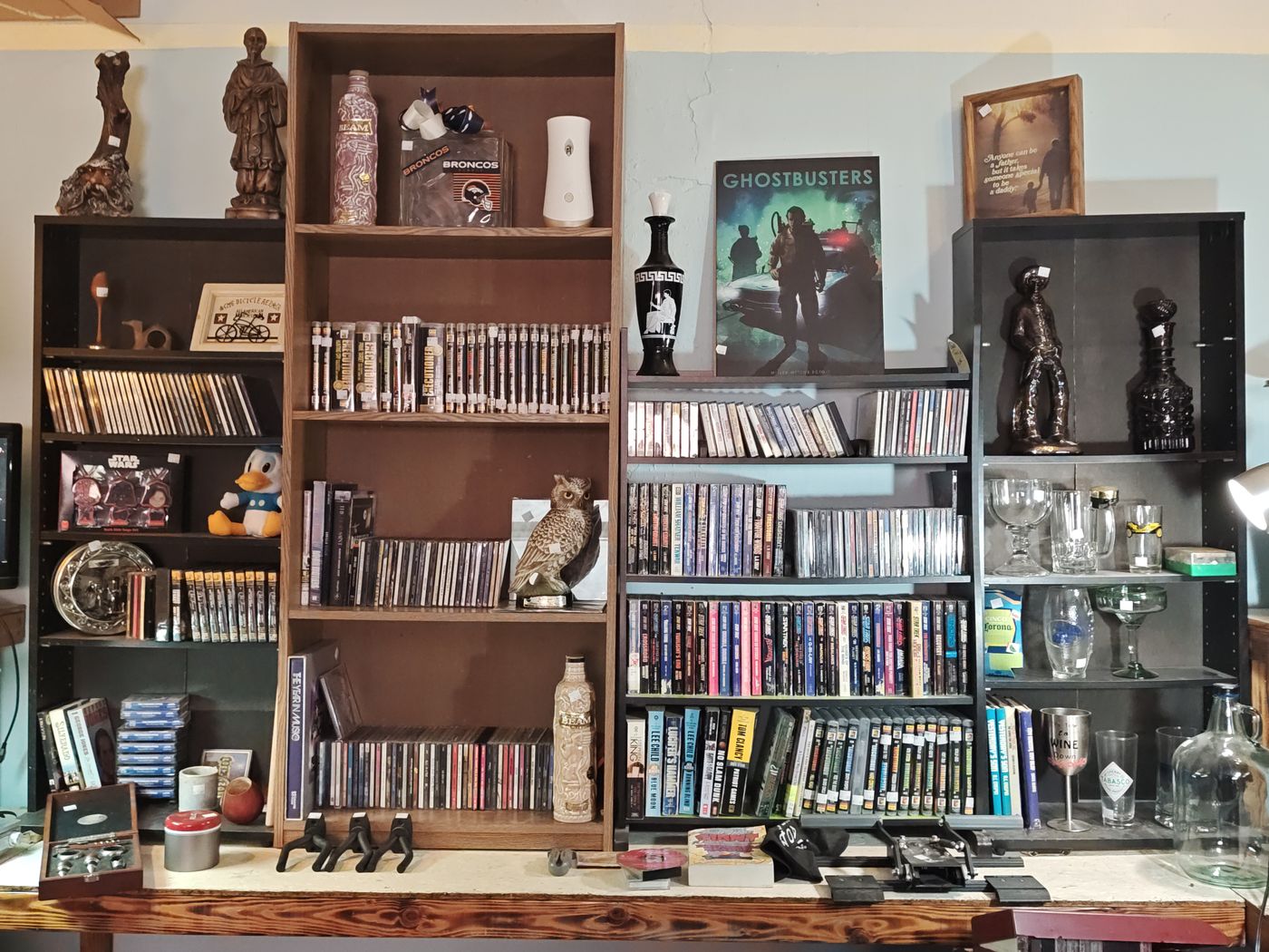 Back wall of shelves with movies, CDs, a Ghostbusters poster, figurines, and glassware