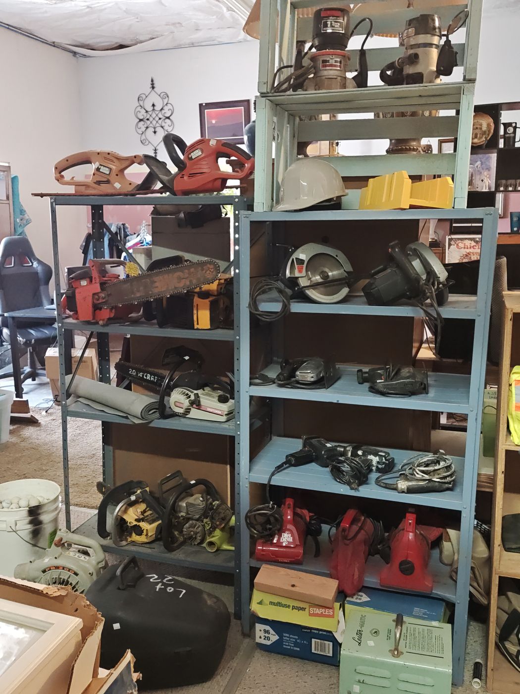 Shelves of power tools and shop gear, including chainsaws, circular saws, routers, and hand vacuums